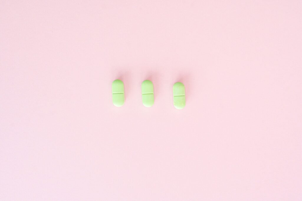 Three green capsules arranged on a pastel pink background, emphasizing minimalism.