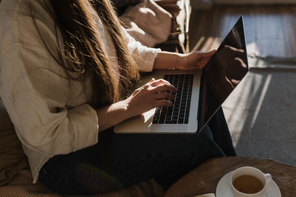 Close-up of a woman using a laptop in a warm, cozy indoor setting with sunlight.